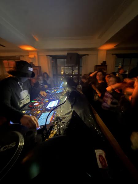 A DJ is actively mixing music on turntables and a mixer, illuminated by colorful lights in a dimly lit room